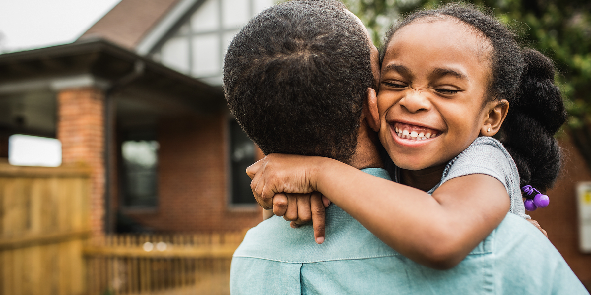 A father and daughter share a heartwarming hug outside their house.