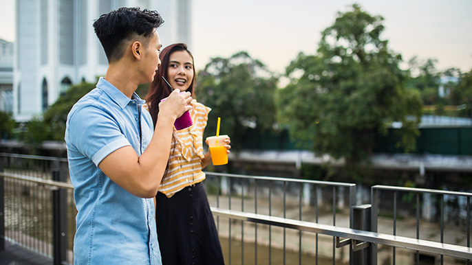 A couple stands on a bridge, holding glasses of orange juice, enjoying a refreshing drink together.