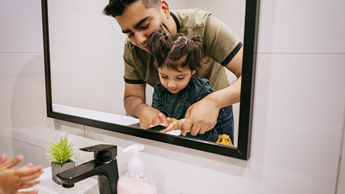 A man and child stand together, gazing at their reflections in a mirror.