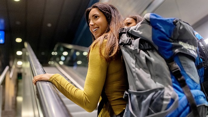 Two women with backpacks navigating an escalator in a bustling city environment.
